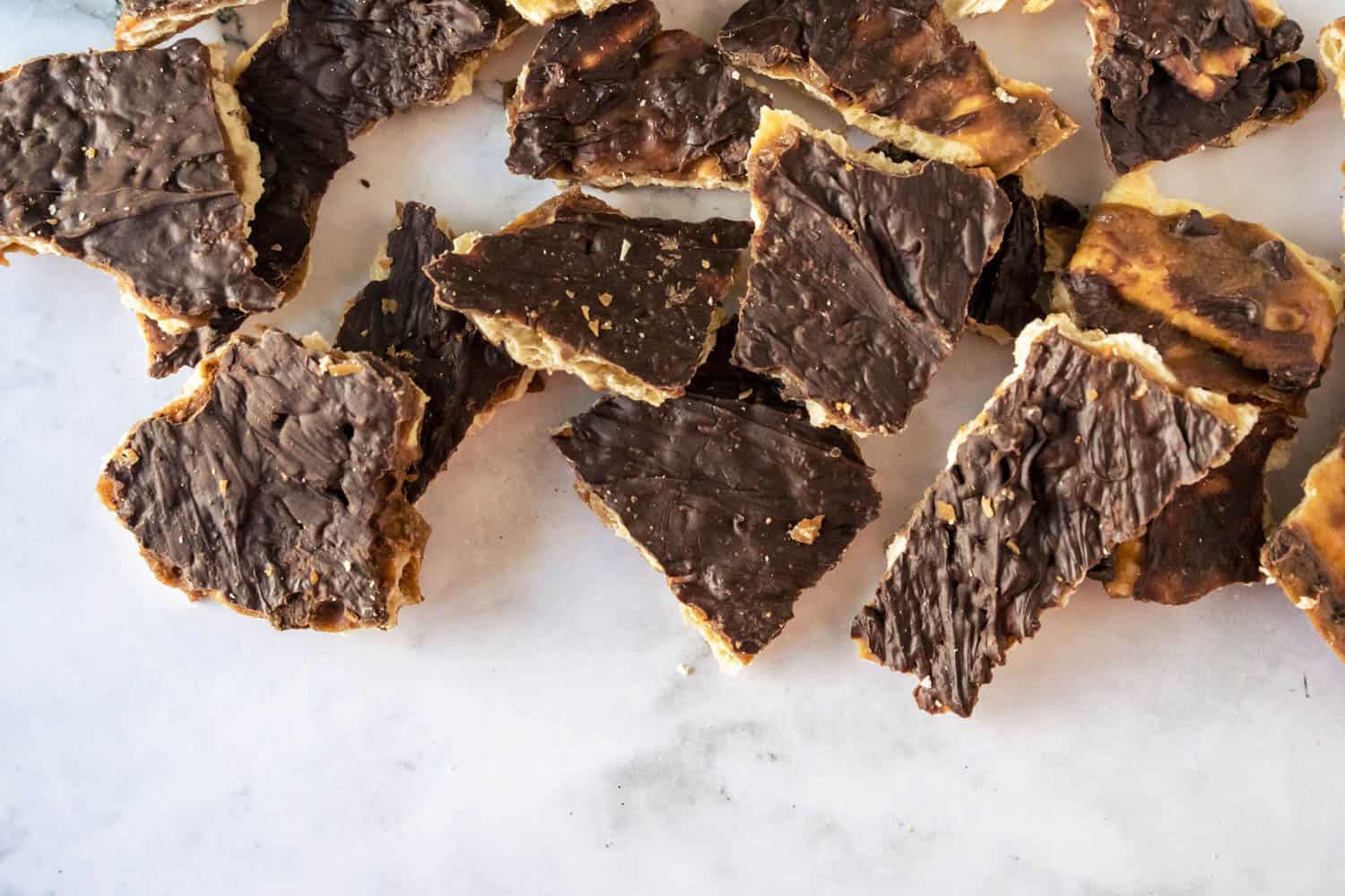 A pile of chocolate-covered pieces of matzo is spread out on a light surface.
