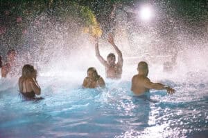 People are enjoying a nighttime pool party with splashing water and bright lights.