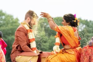 A bride in a traditional saree pours rice over the groom's head during a wedding ceremony.