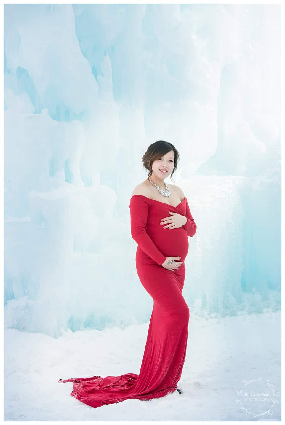 Woman and daughter post in red dresses for maternity portraits at the Ice Castles in New Hampshire