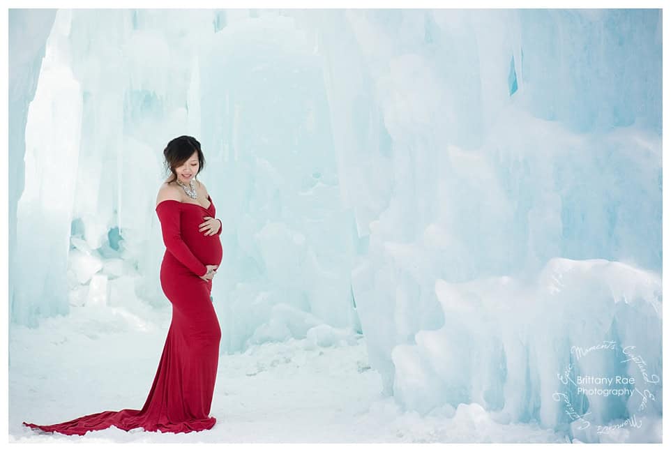 Woman and daughter post in red dresses for maternity portraits at the Ice Castles in New Hampshire