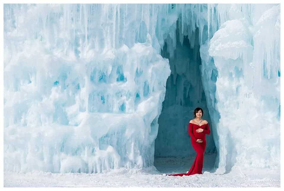 Woman and daughter post in red dresses for maternity portraits at the Ice Castles in New Hampshire