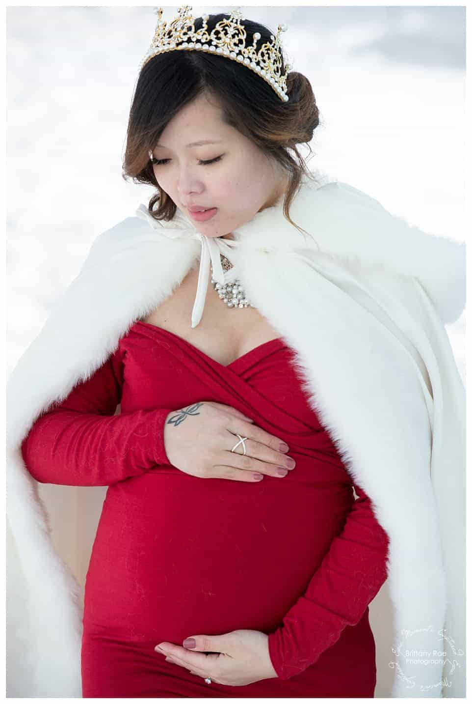 Woman and daughter post in red dresses for maternity portraits at the Ice Castles in New Hampshire