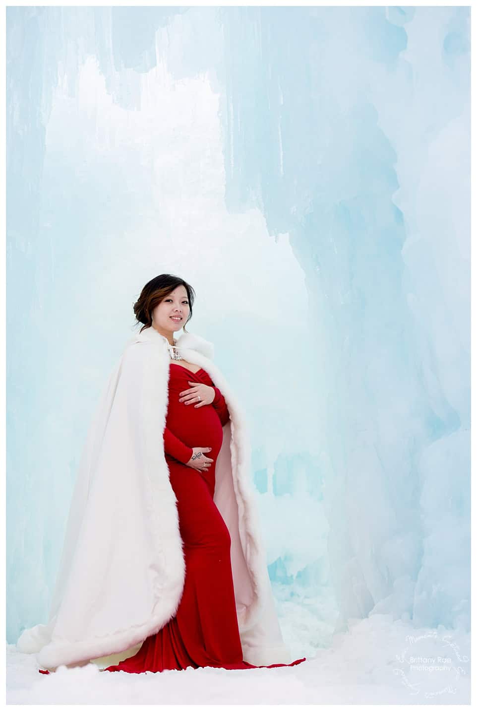 Woman and daughter post in red dresses for maternity portraits at the Ice Castles in New Hampshire