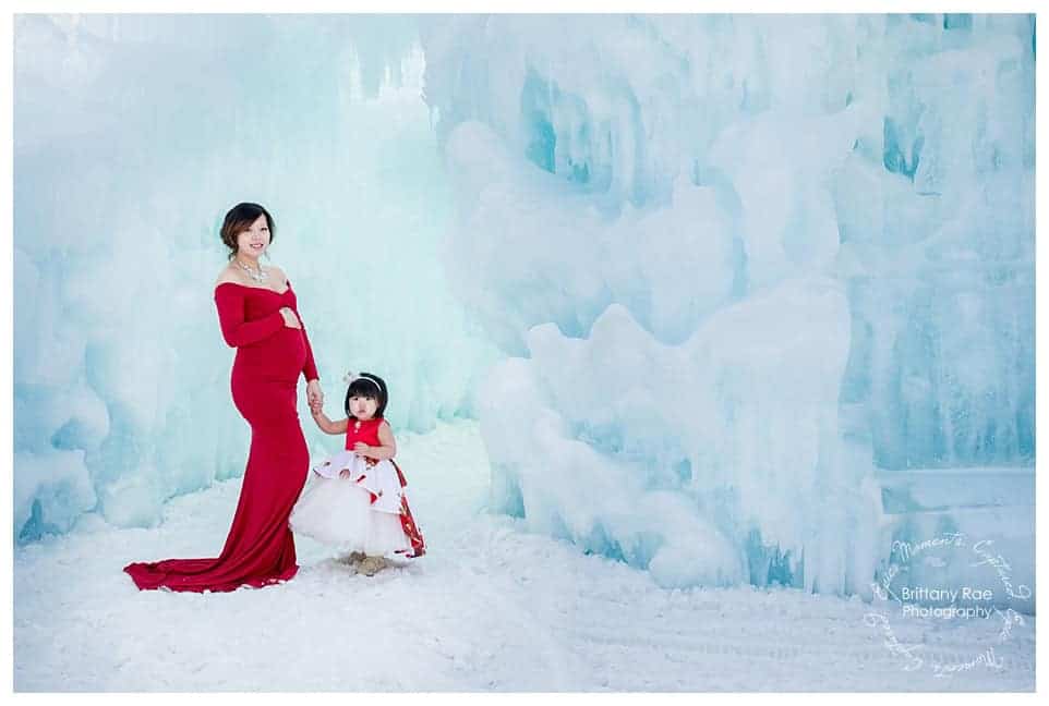 Woman and daughter post in red dresses for maternity portraits at the Ice Castles in New Hampshire